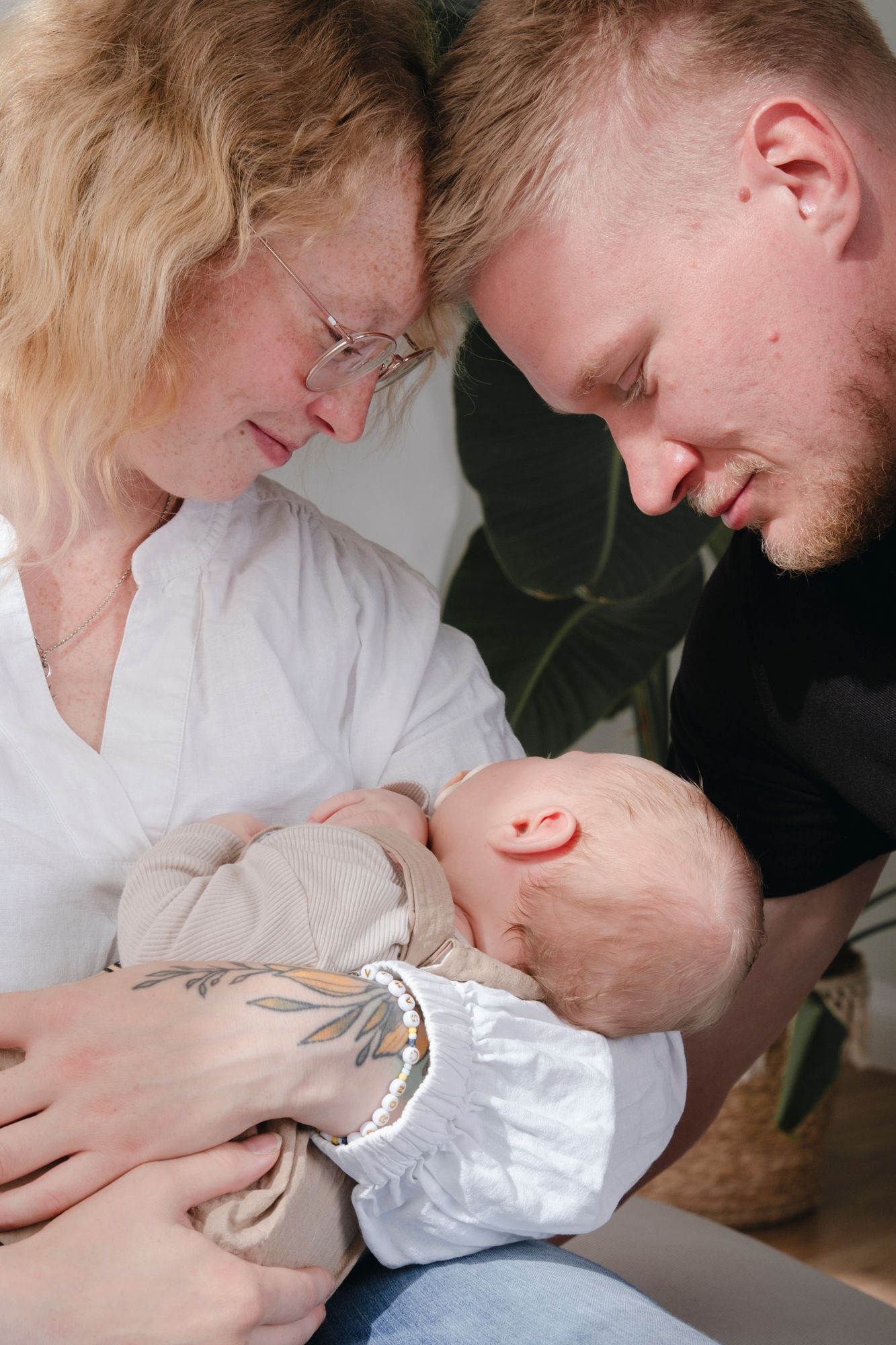 Loving parents leaning in close together while cradling their newborn baby indoors.