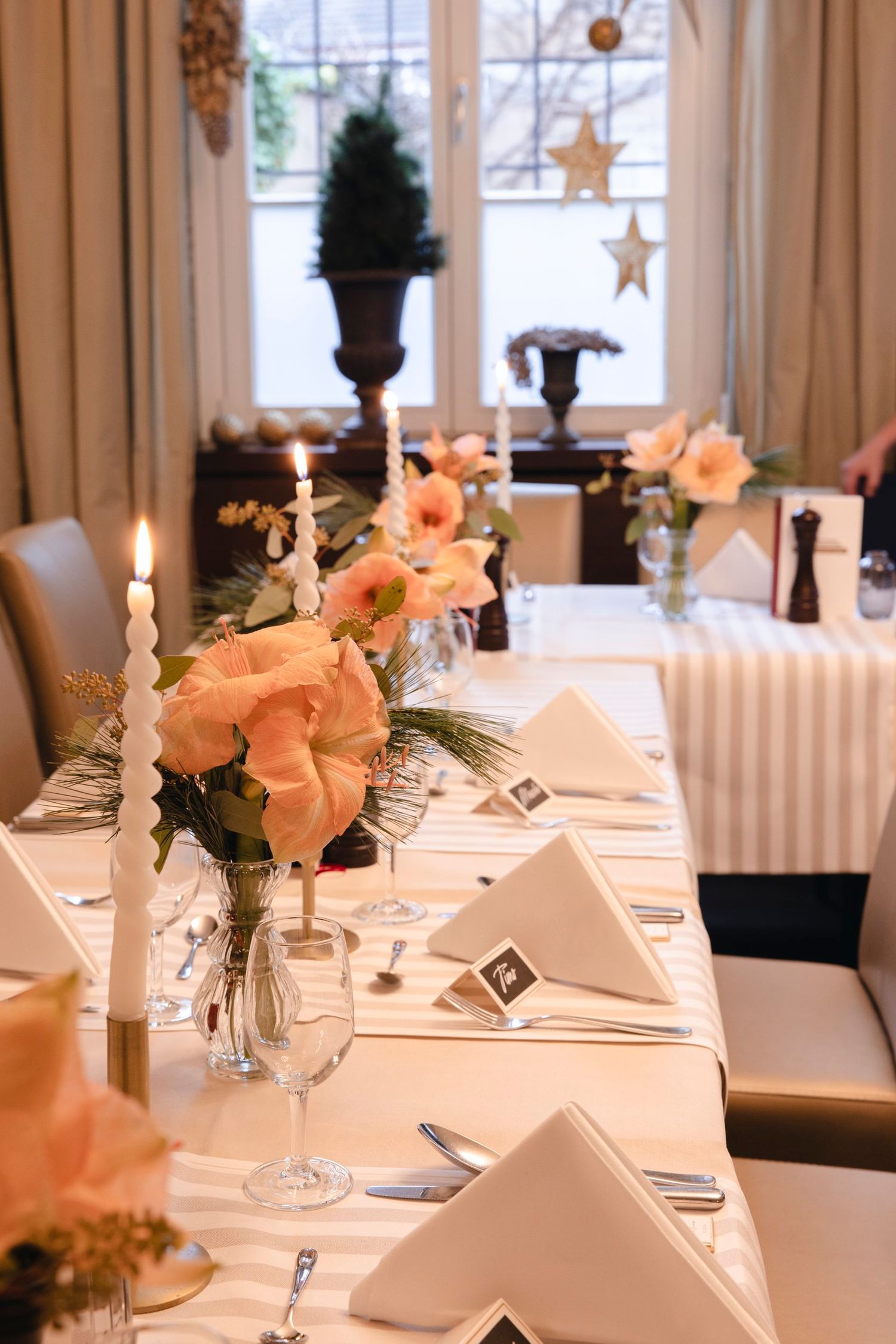 Romantic wedding reception table with peach roses, lit taper candles, white napkins and gold star decor.