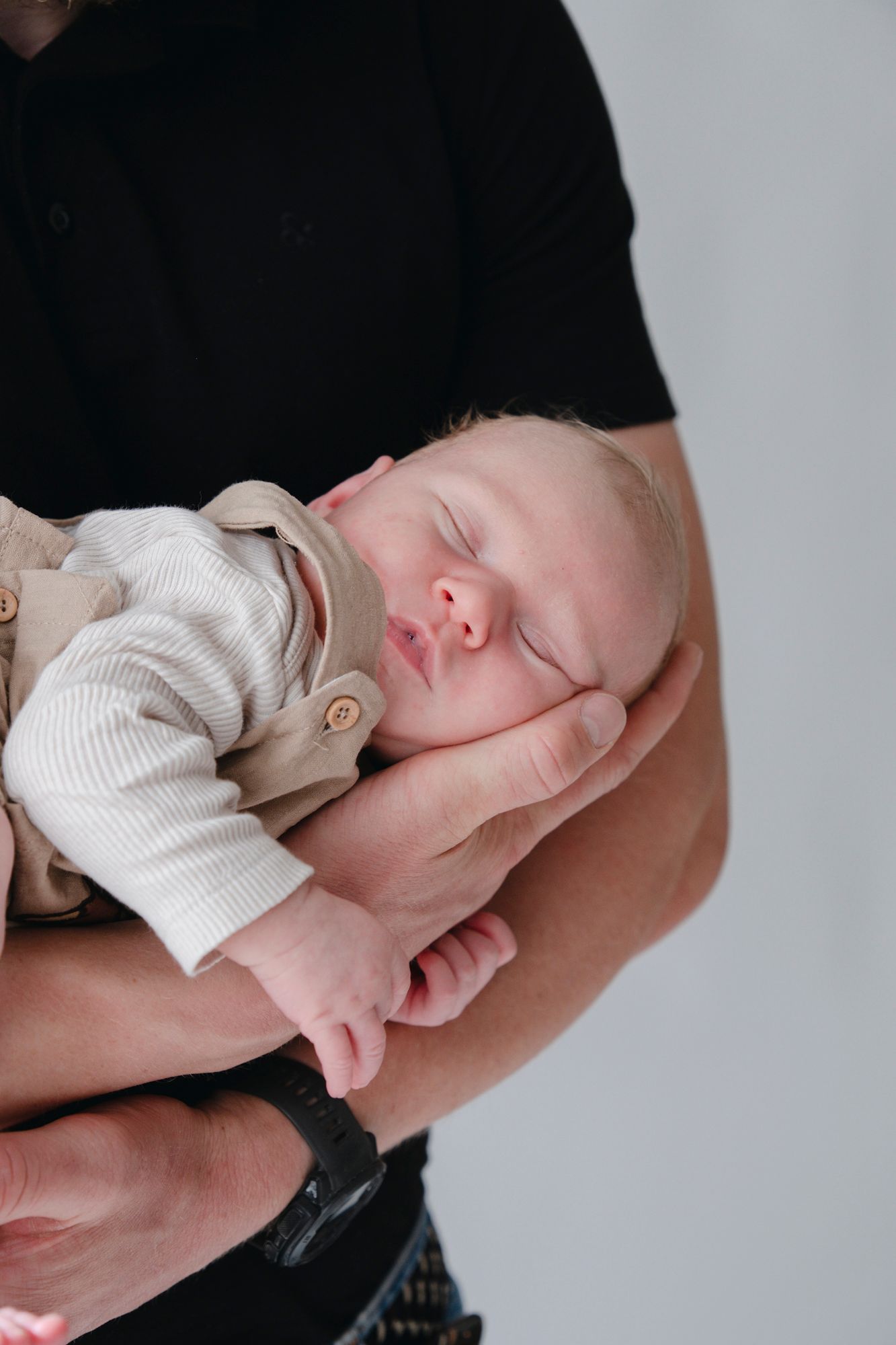 Newborn baby sleeping peacefully cradled in father's strong hands against white background.