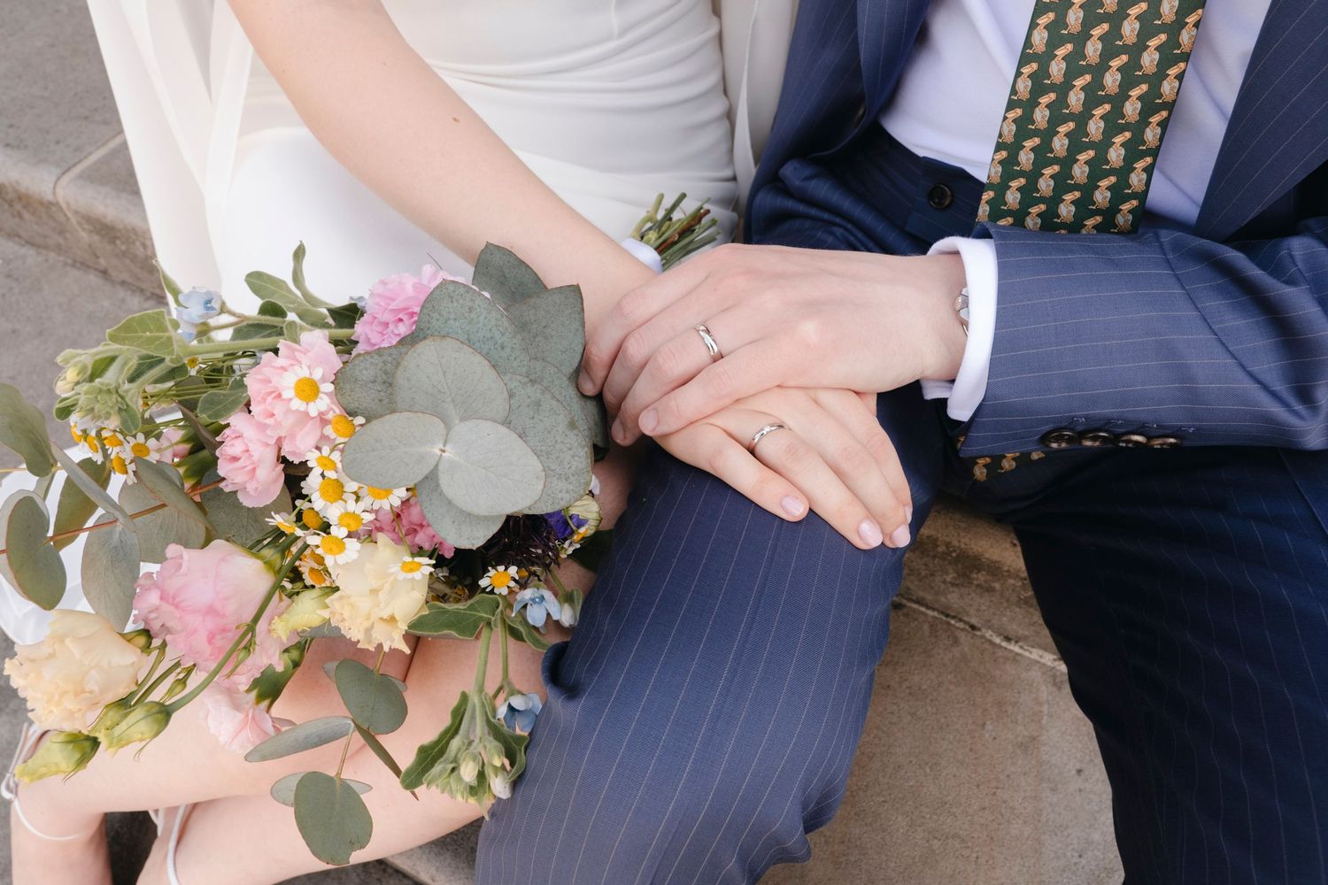 Close-up of newlywed couple's hands showing wedding rings with a colorful bridal bouquet.