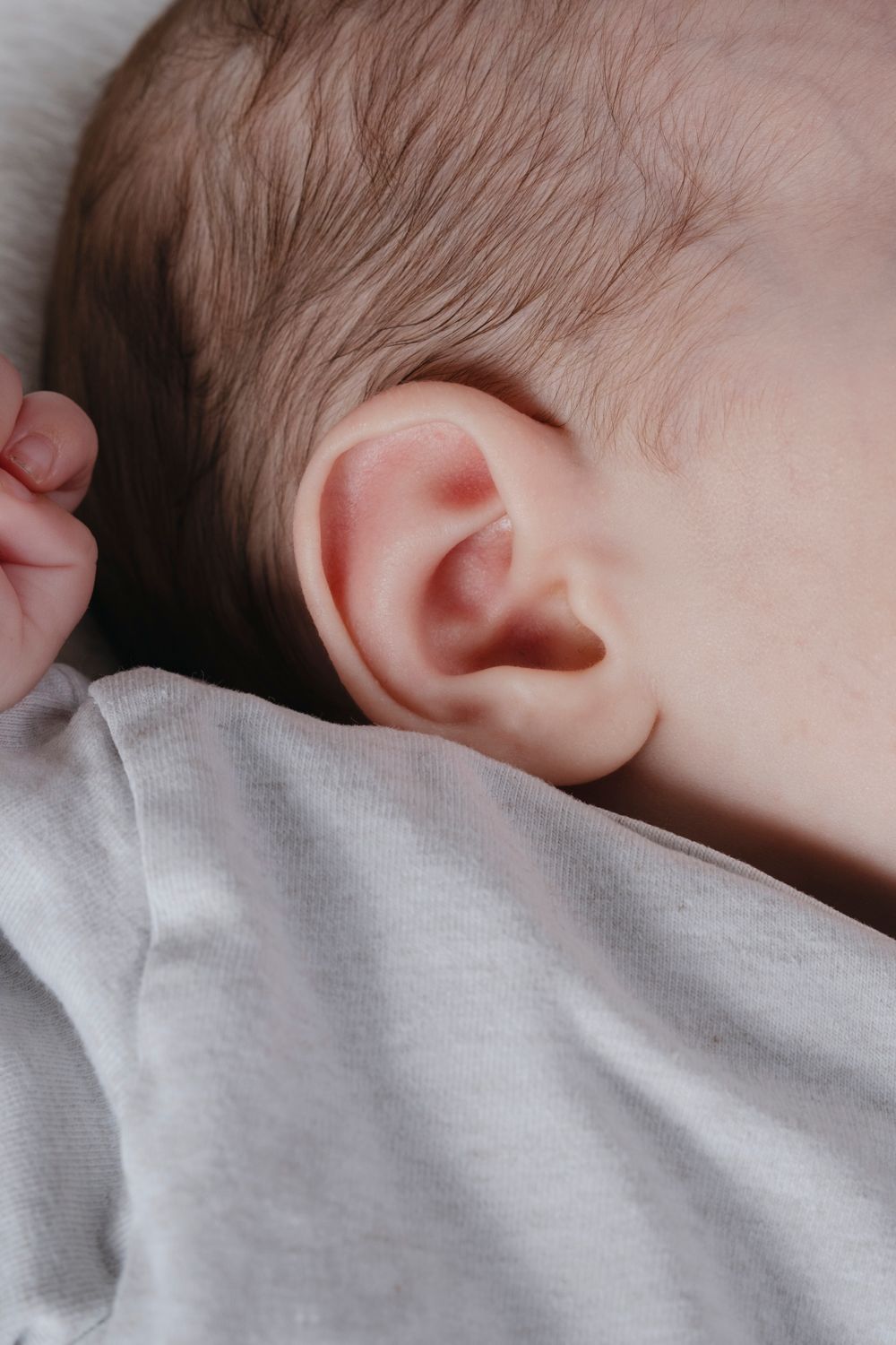 Close-up of a newborn baby's ear with fine hair visible, lying on a soft white surface.