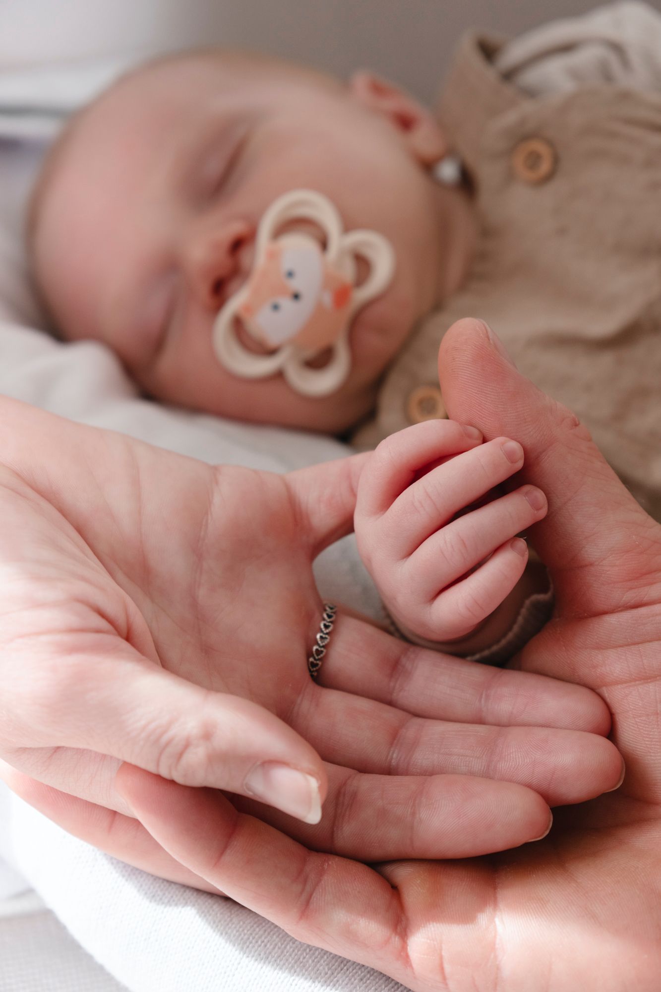 Sleeping newborn with pacifier resting small hand in mother's gentle cupped palms.