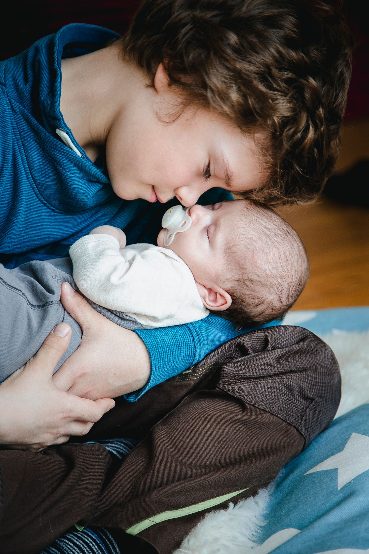 Young boy tenderly kissing newborn baby sibling on the forehead.