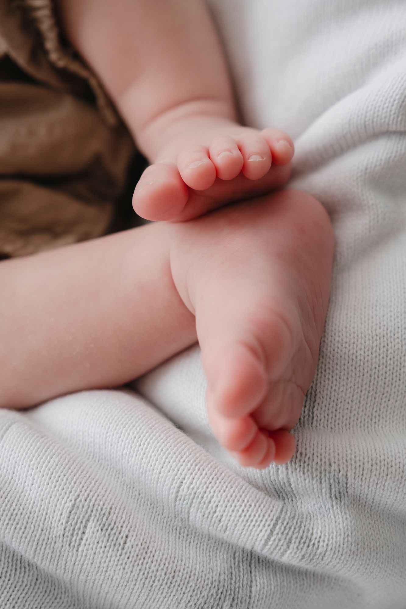 Close-up of tiny newborn baby feet resting softly on a white knit blanket.