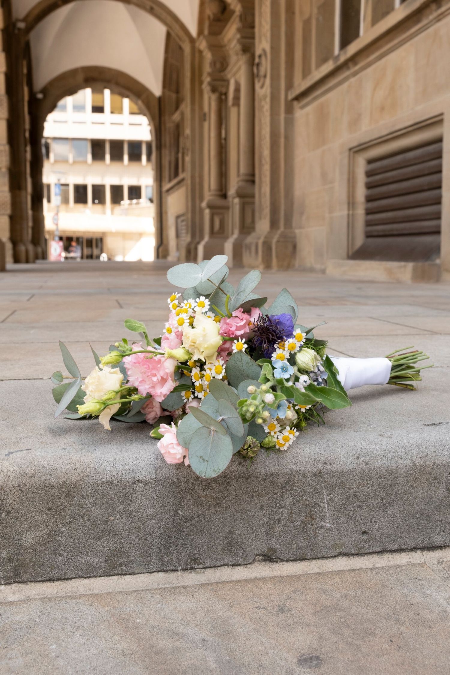 Colorful bridal bouquet with pink roses, daisies, and eucalyptus resting on stone steps.