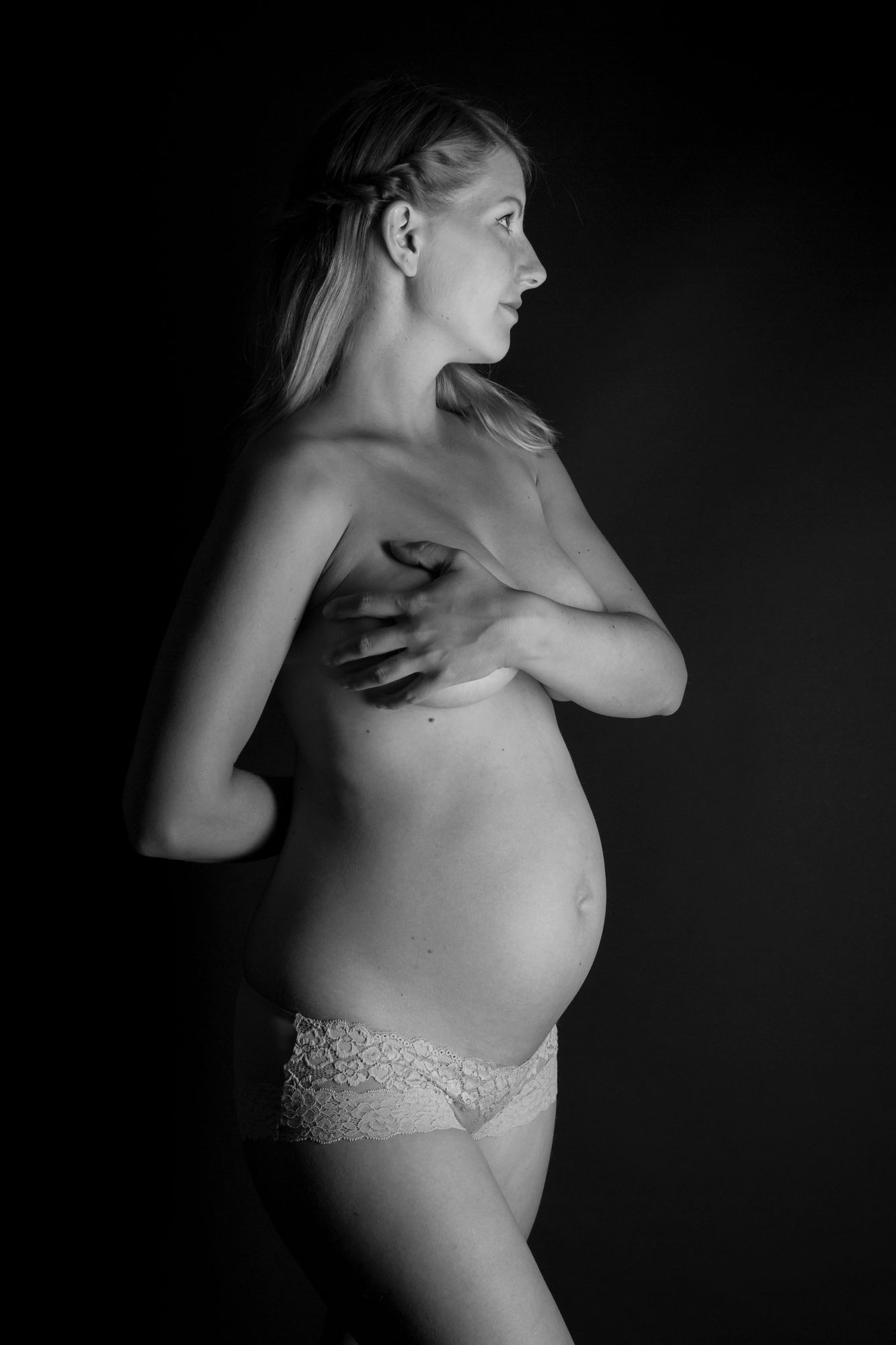 Black and white side profile of a topless pregnant woman cradling her bare baby bump.