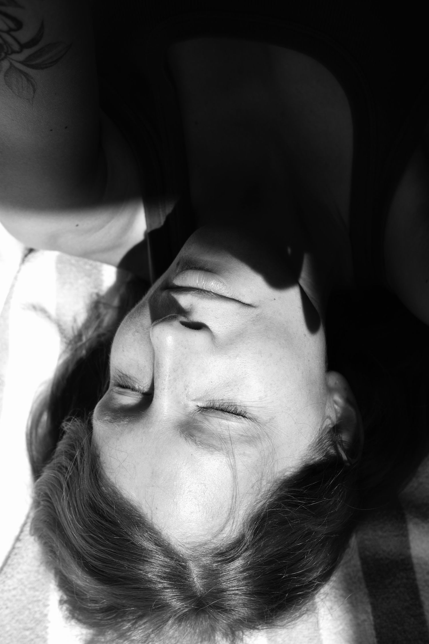 Black and white portrait of a woman with closed eyes, photographed from above in dramatic lighting.