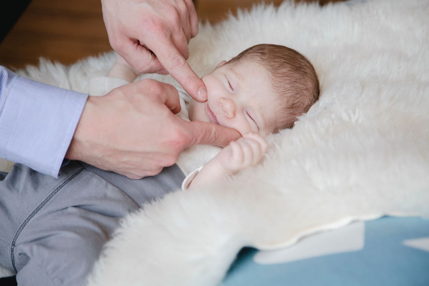 Parent gently touching sleeping newborn baby on fluffy white blanket.
