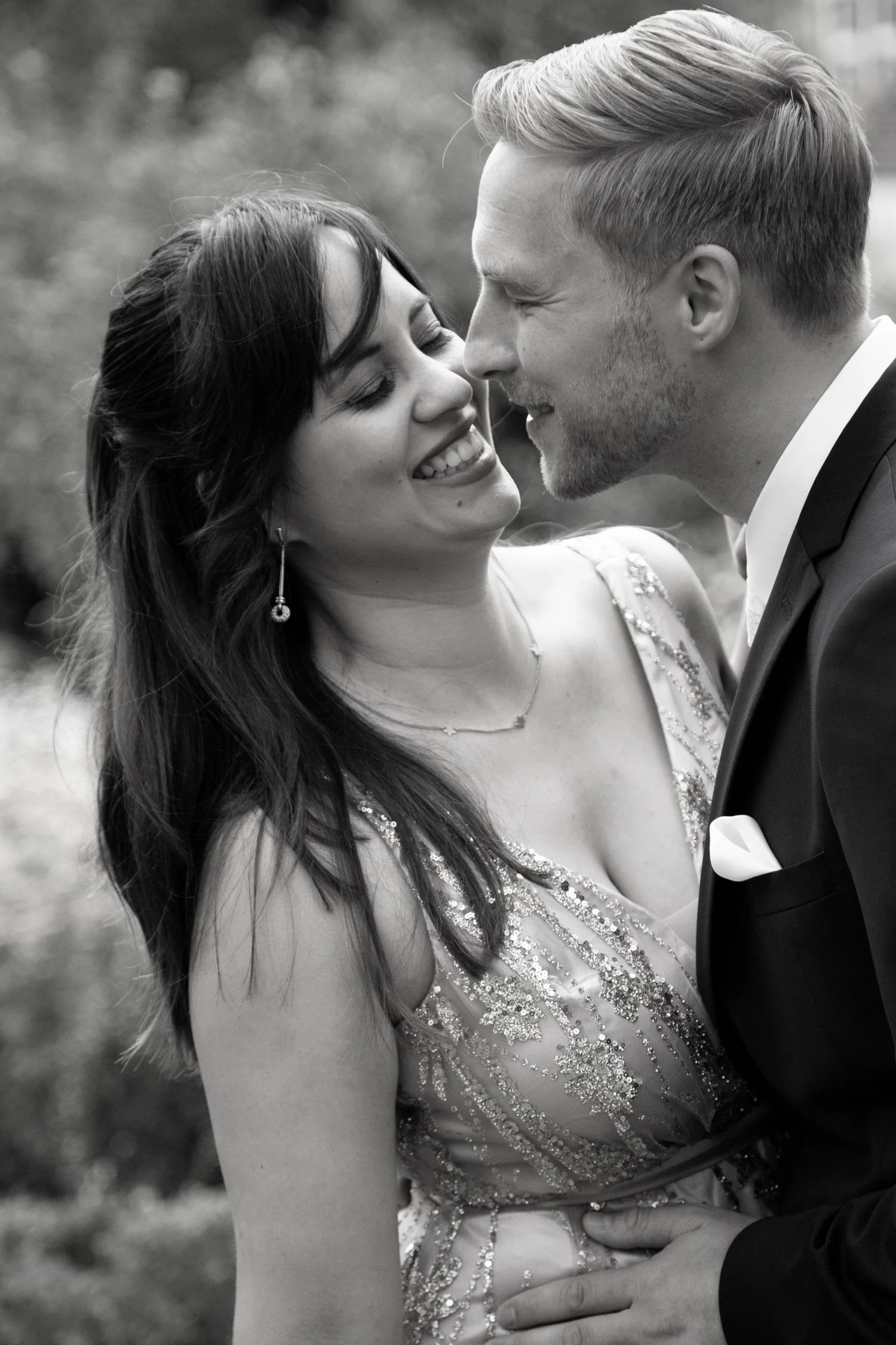 Joyful couple in formal attire sharing an intimate moment outdoors, black and white portrait.