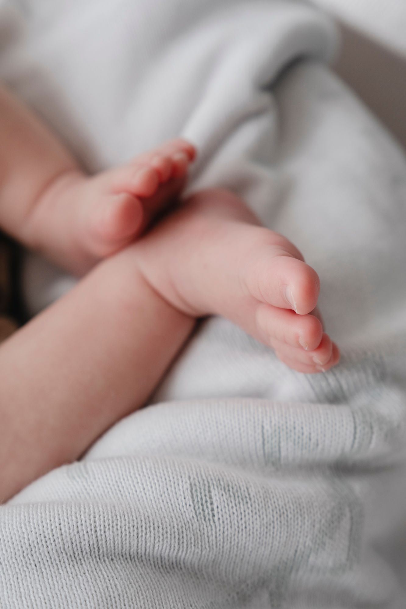 Close-up of tiny newborn baby feet resting on a soft grey blanket.