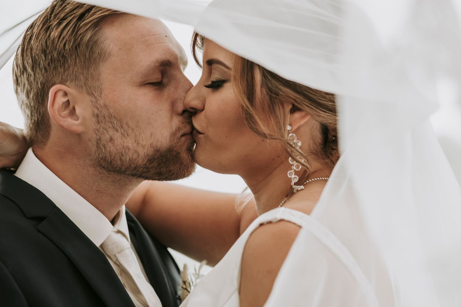 Close-up of bride and groom sharing romantic kiss under flowing white veil on wedding day.