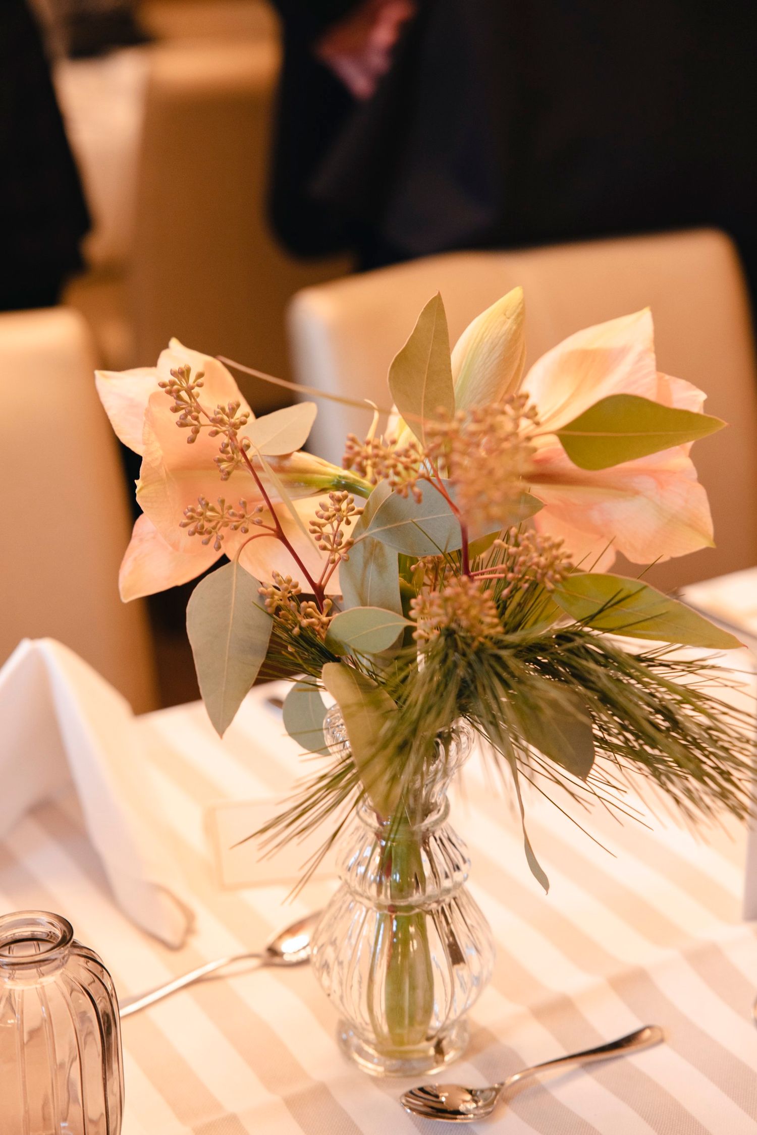 Delicate wedding centerpiece with blush amaryllis, eucalyptus and pine stems in glass bud vase.