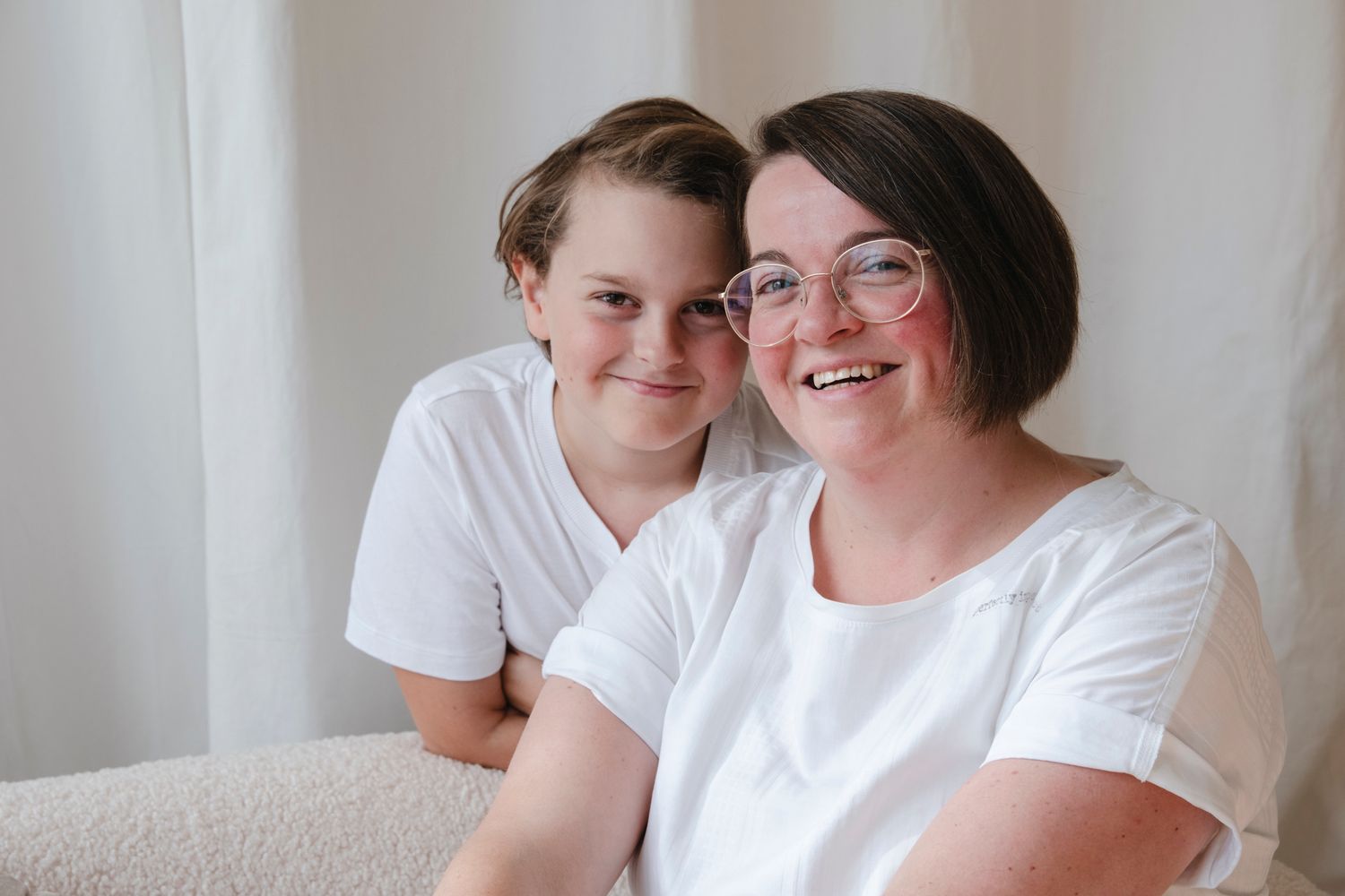 Smiling mother and preteen son posing together in white shirts.