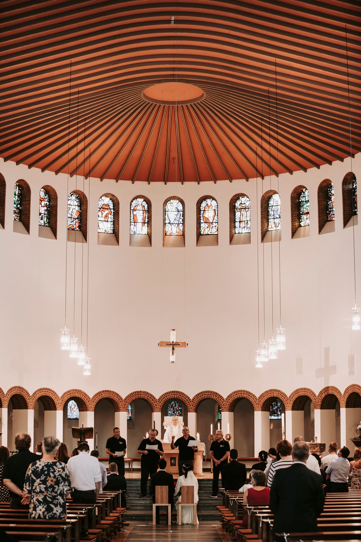 Interior of modern circular church with stained glass windows during wedding ceremony with guests seated.