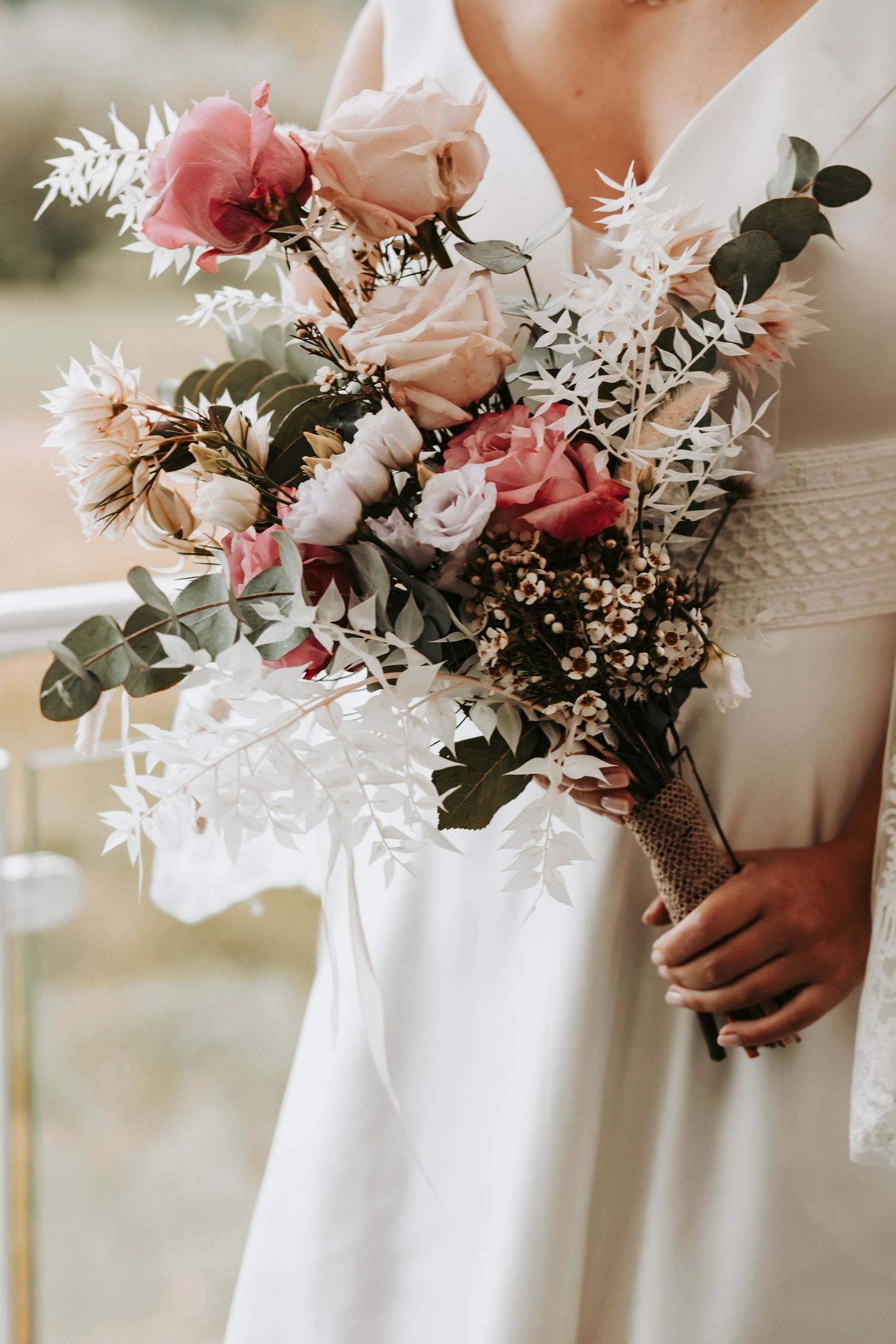 Bride holding a romantic wedding bouquet with pink roses, dried flowers, and eucalyptus in a burlap wrap.
