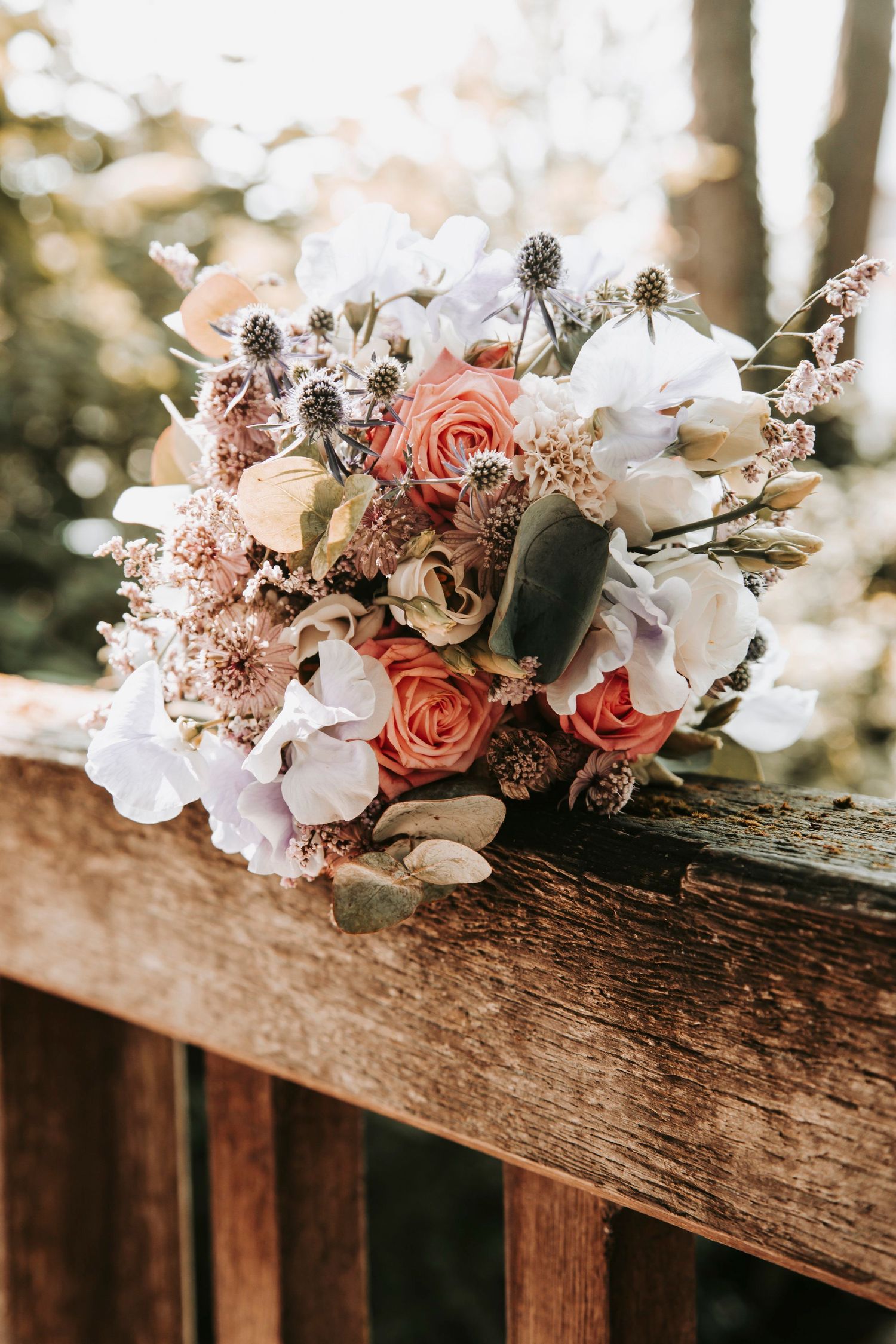 Elegant bridal bouquet with pink roses, white hydrangeas, and wildflowers resting on wooden fence.