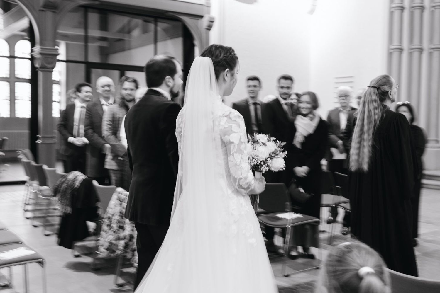 Black and white wedding photo of bride and groom walking down church aisle with raised hands.