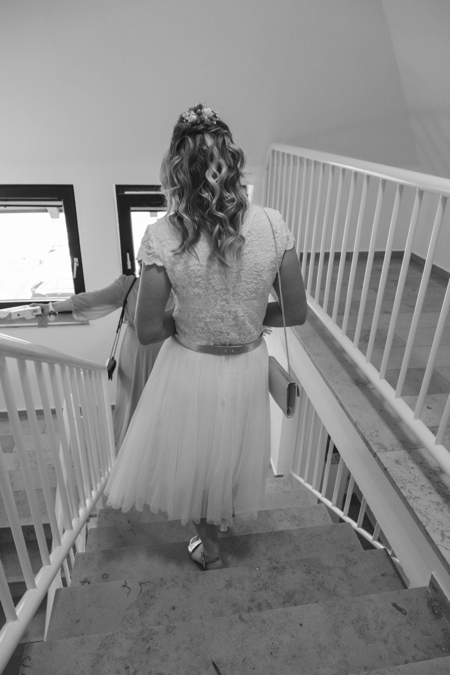 Black and white rear view of a flower girl in a white tulle dress walking up stairs.