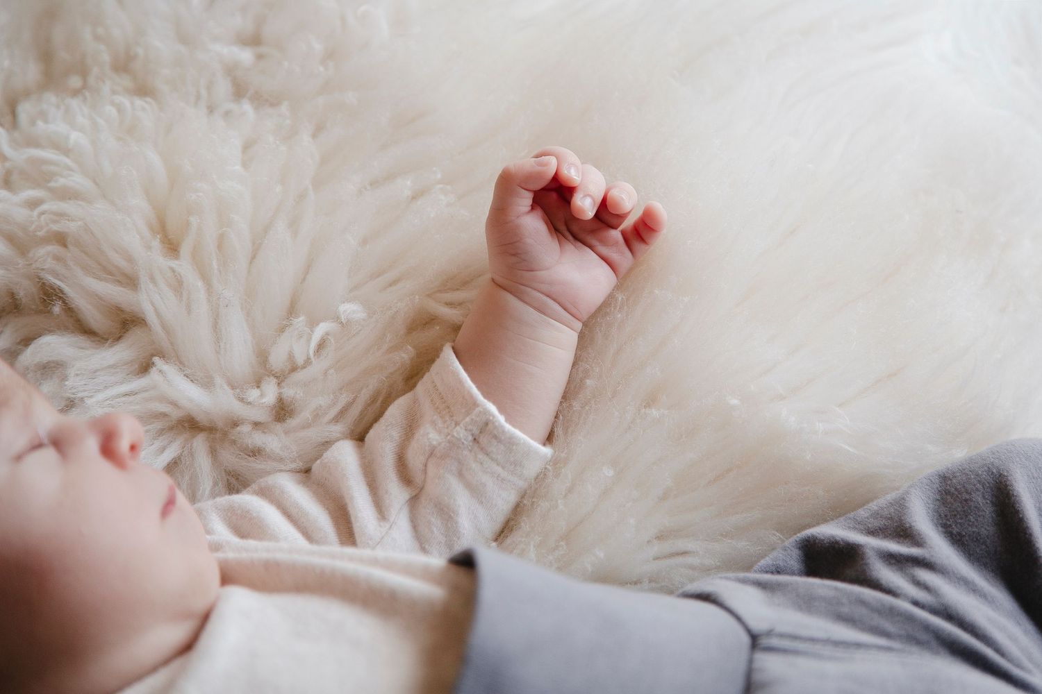 Close-up of a newborn baby's tiny hand resting on a soft white fluffy rug.
