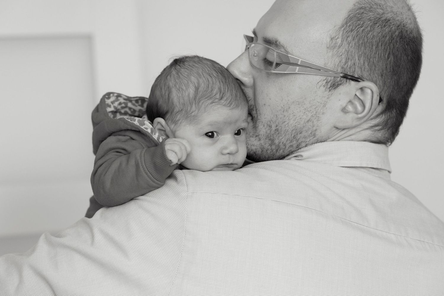 Father kissing his newborn baby on the head in a tender black and white portrait.