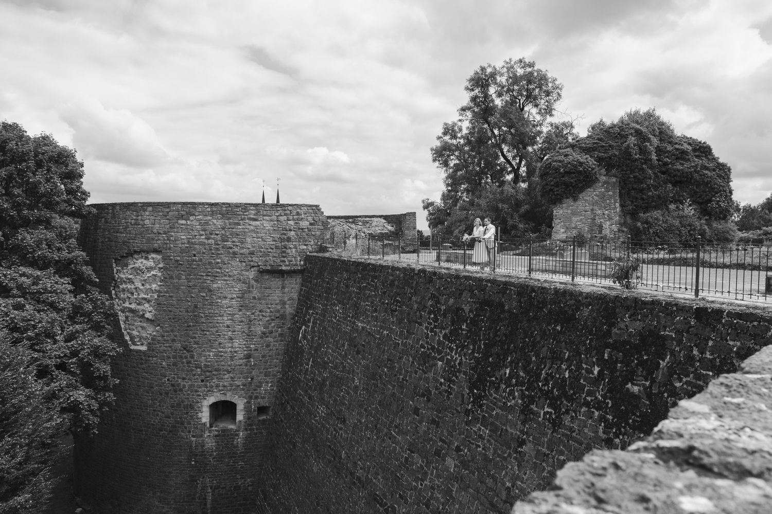 Black and white aerial view of historic stone castle walls and bridge with couple walking.