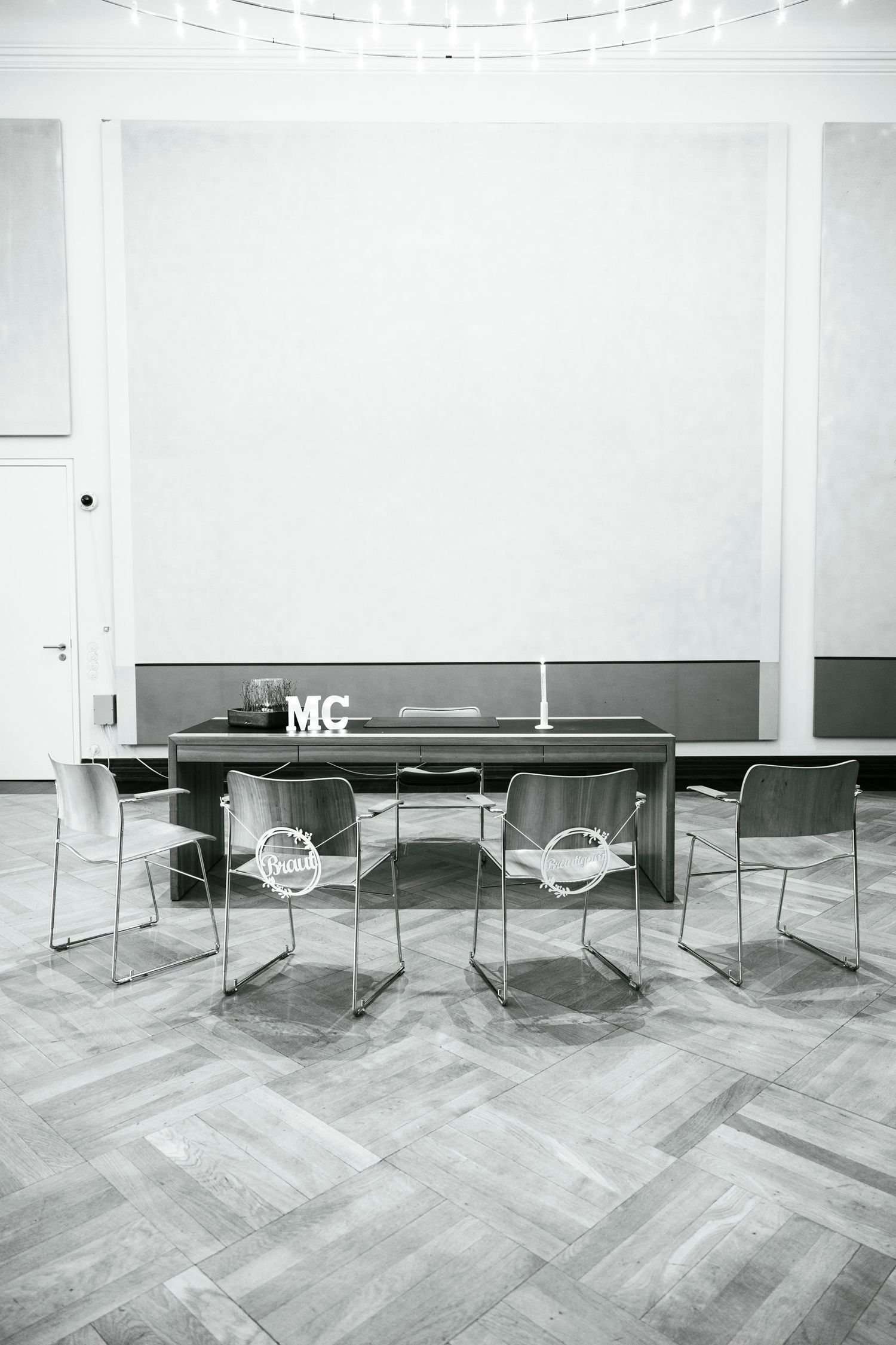 Black and white photo of empty civil registry wedding room with transparent chairs and decorated table with MC letters.