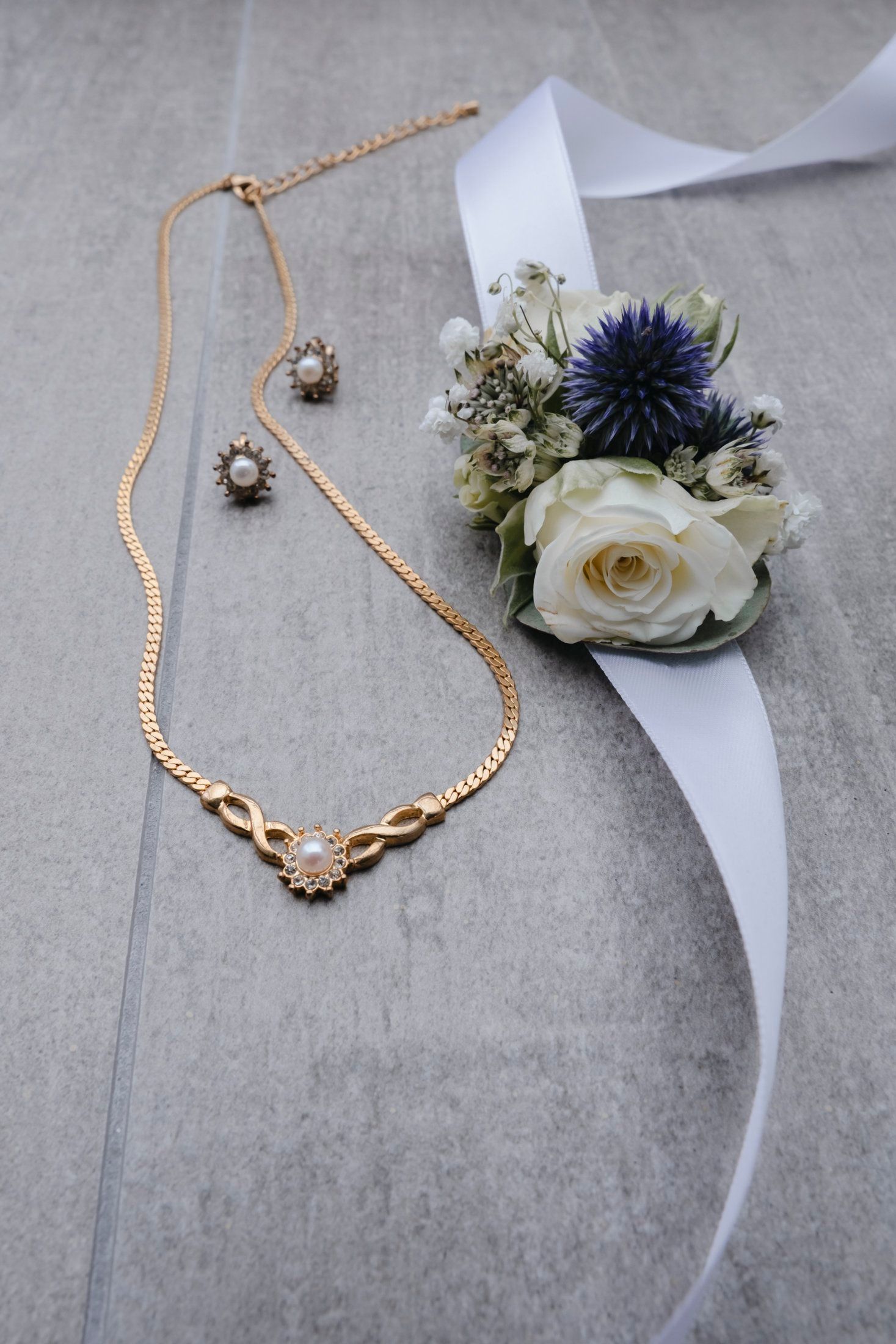 Gold pearl necklace and earrings set beside a white rose and blue thistle wedding corsage.
