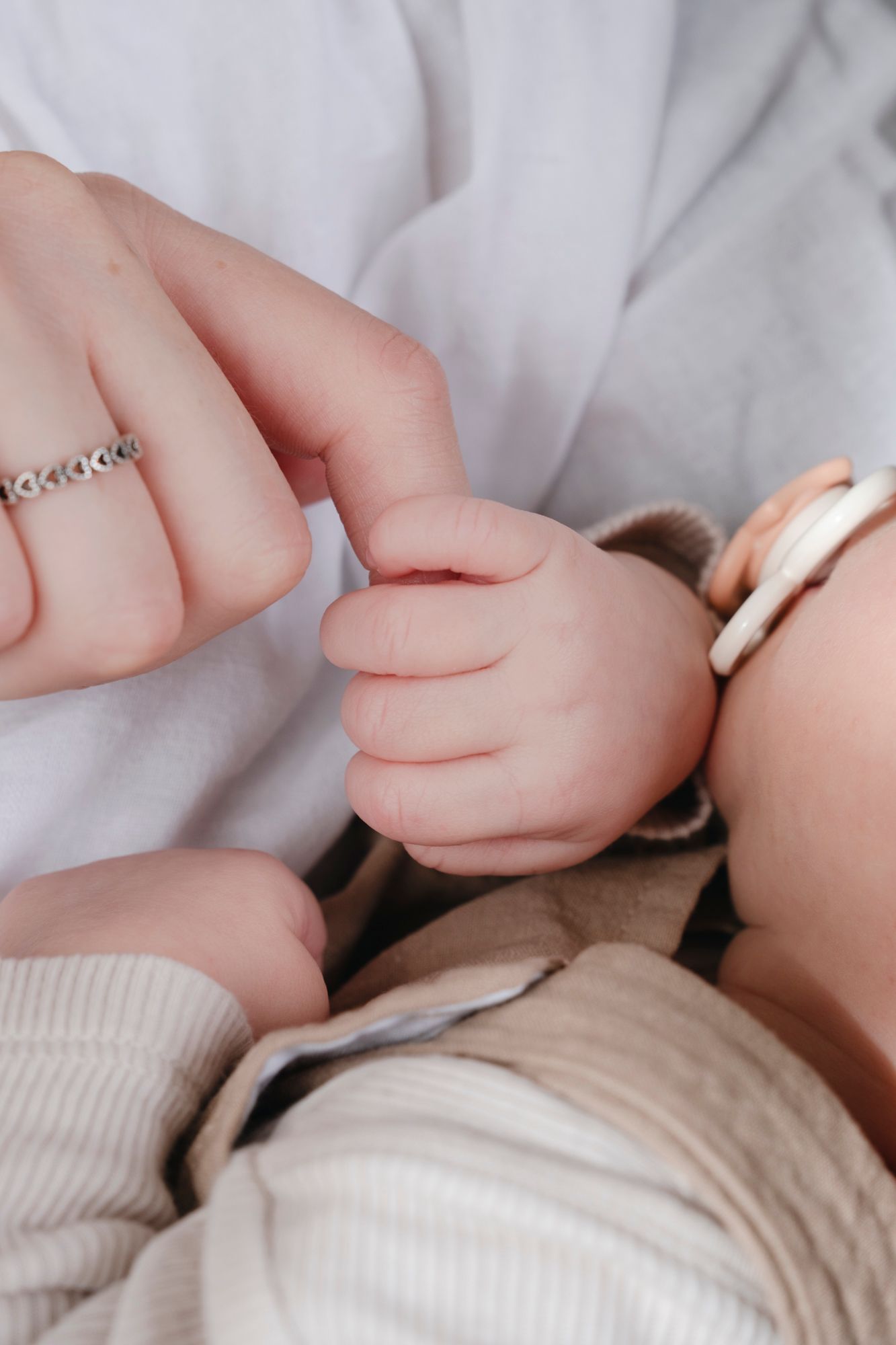 Close-up of a newborn baby grasping an adult finger, with mother wearing a delicate silver ring.