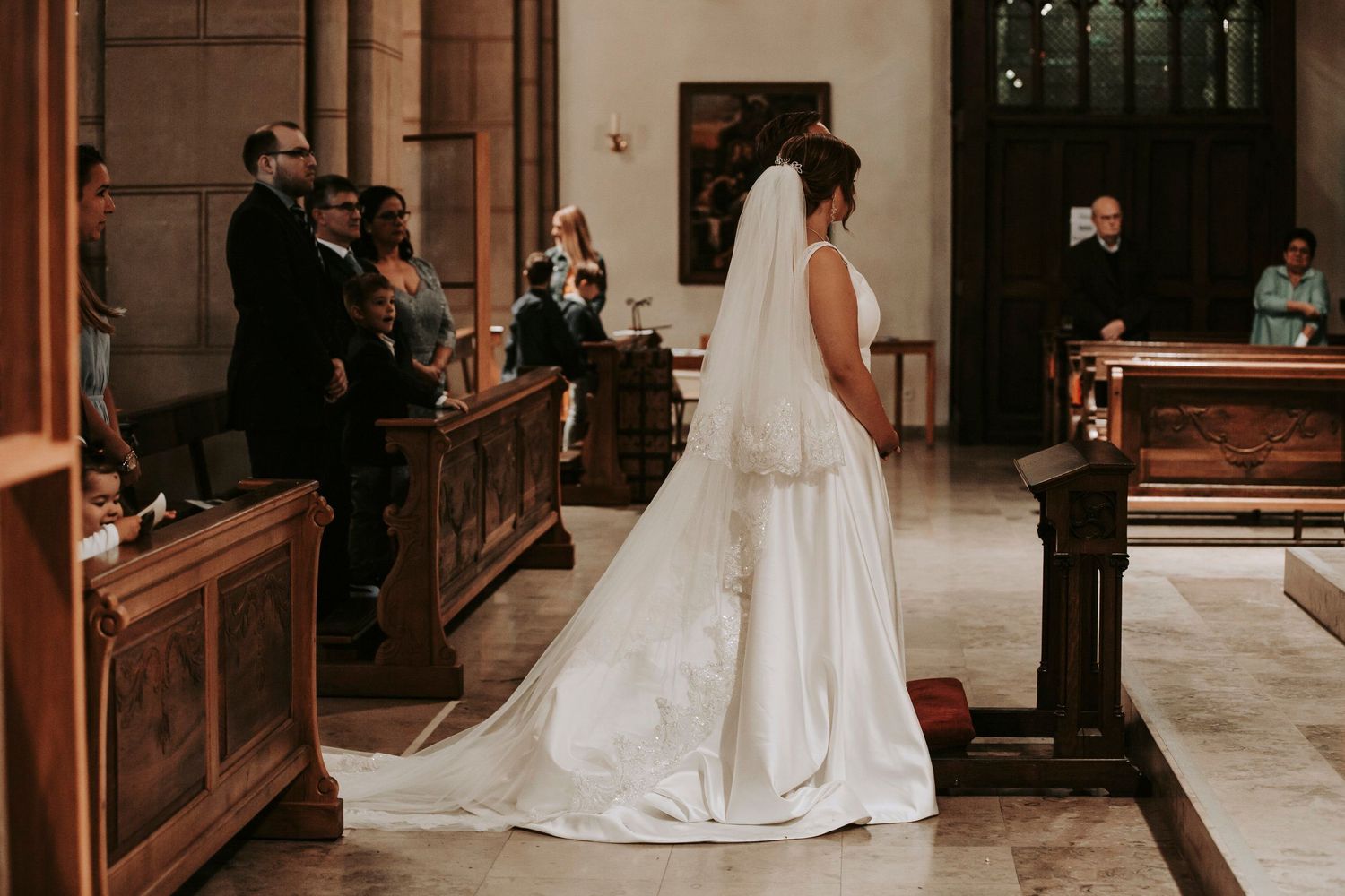 Bride in white gown with long veil standing at church altar during wedding ceremony.