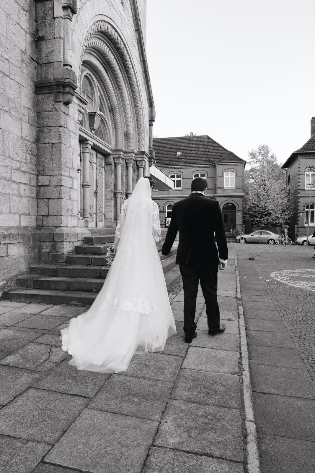 Bride and groom walk hand in hand away from a historic stone church in a classic black and white wedding photo.