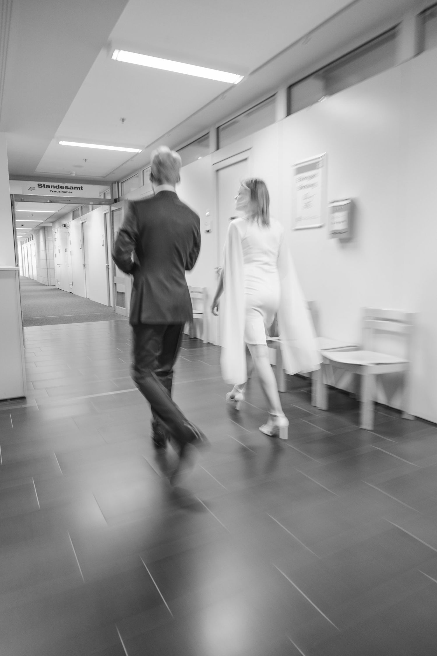 Motion-blurred black and white photo of a couple walking down a corridor toward the Standesamt registry office.
