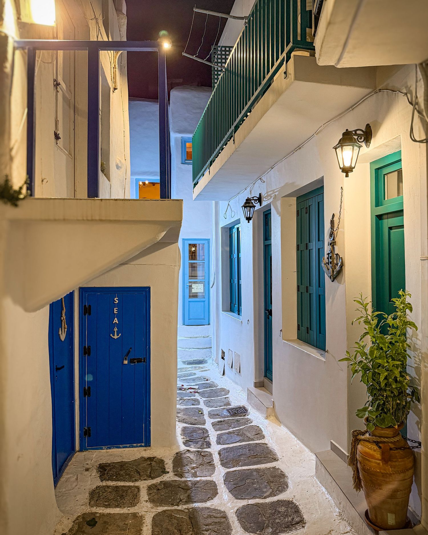 Narrow whitewashed alley with a blue door illuminated at night in Mykonos Town, Greece