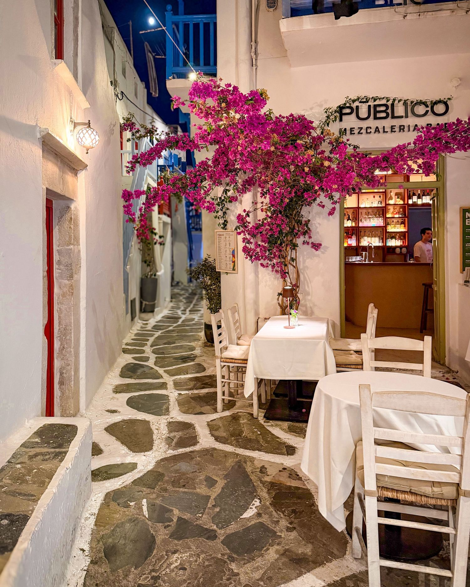 Bougainvillea-lined lane with outdoor restaurant seating in Mykonos Town, Greece