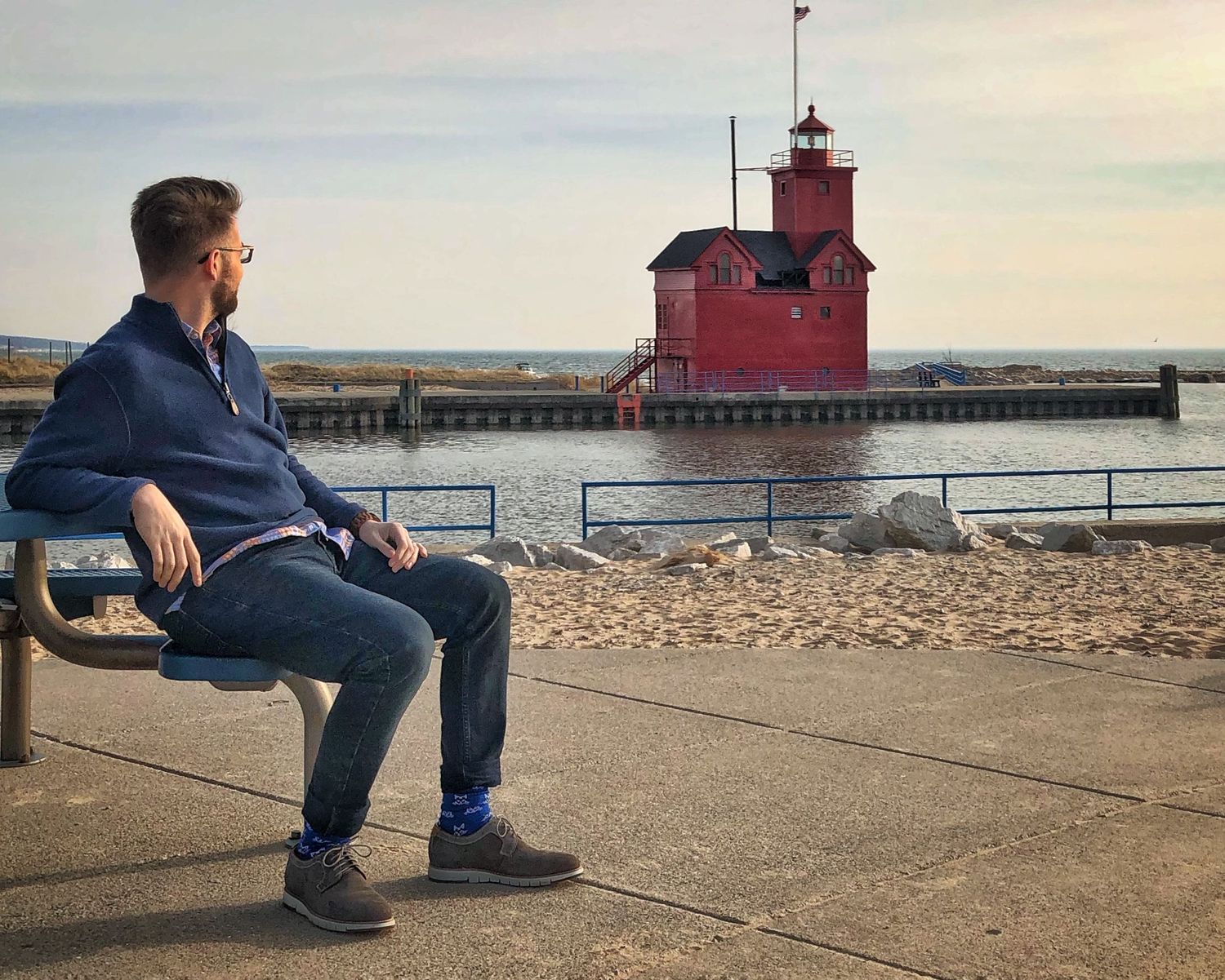 Tim sitting on a dockside park bench looking toward Big Red Lighthouse in Holland, Michigan