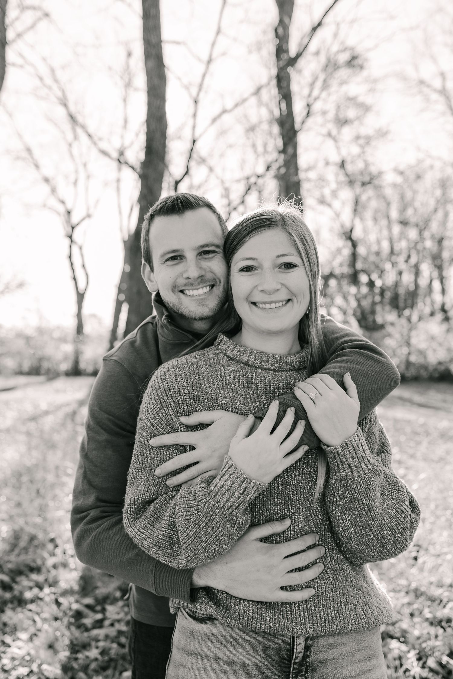 A couple embraces outdoors in black and white photos showing playful and romantic moments in a wooded setting.