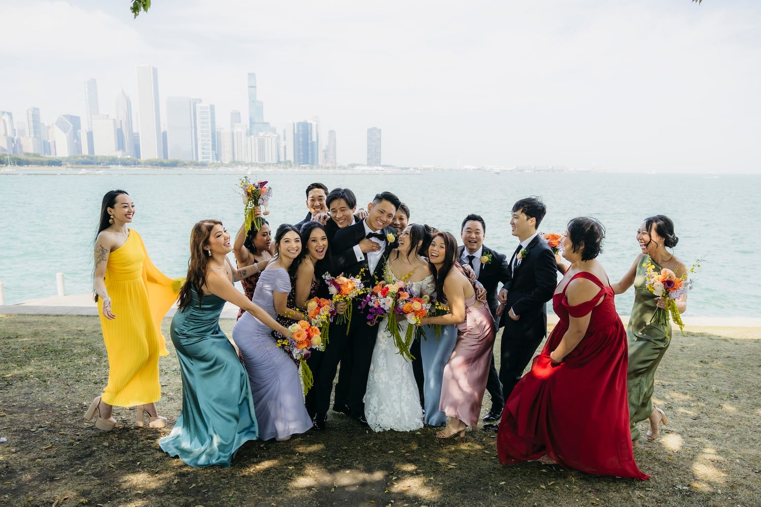 A joyful wedding party in colorful gowns celebrates with the Chicago skyline and lake in background.
