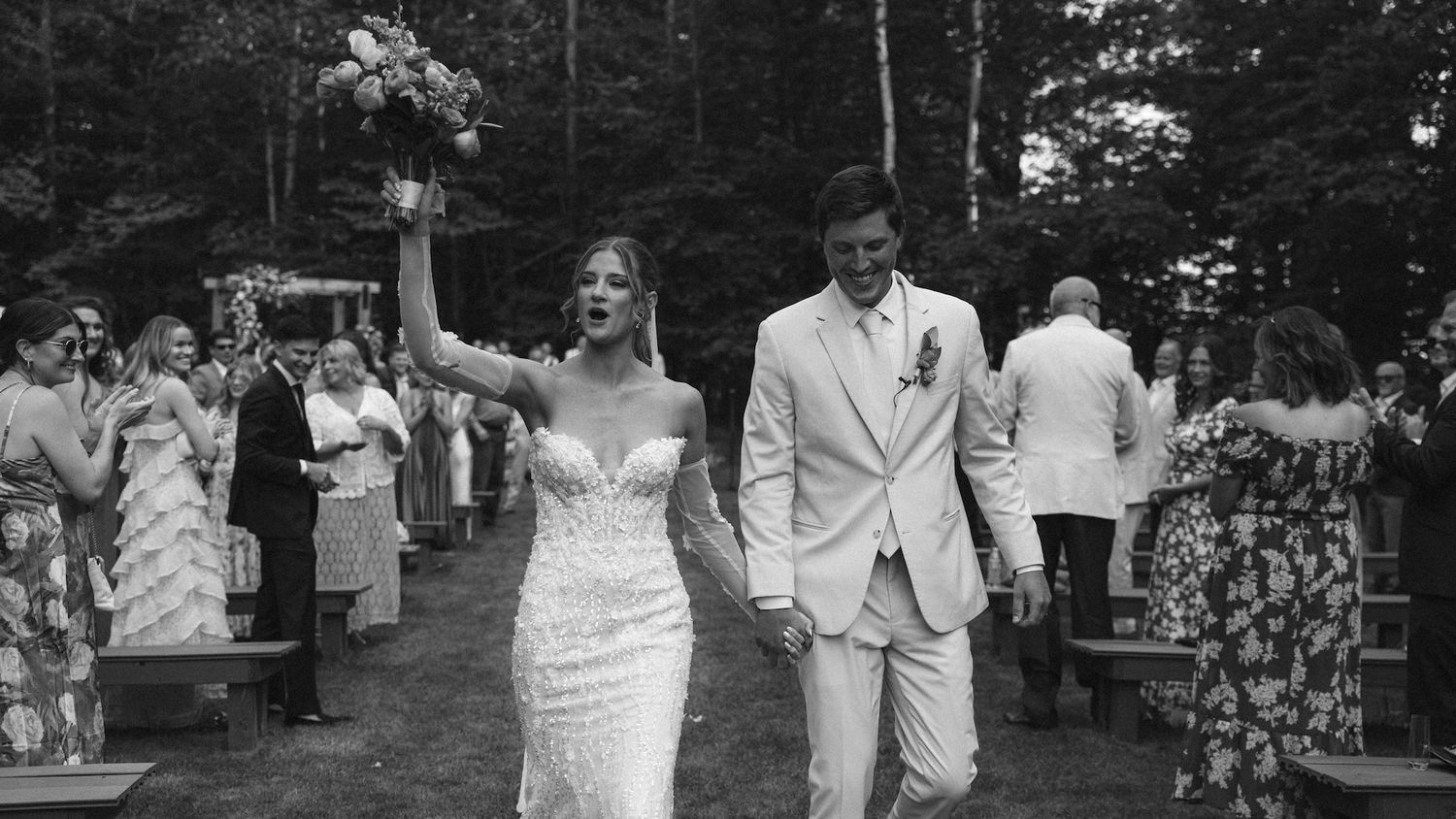 Black and white photo of a bride and groom walking down the aisle after their outdoor wedding ceremony.