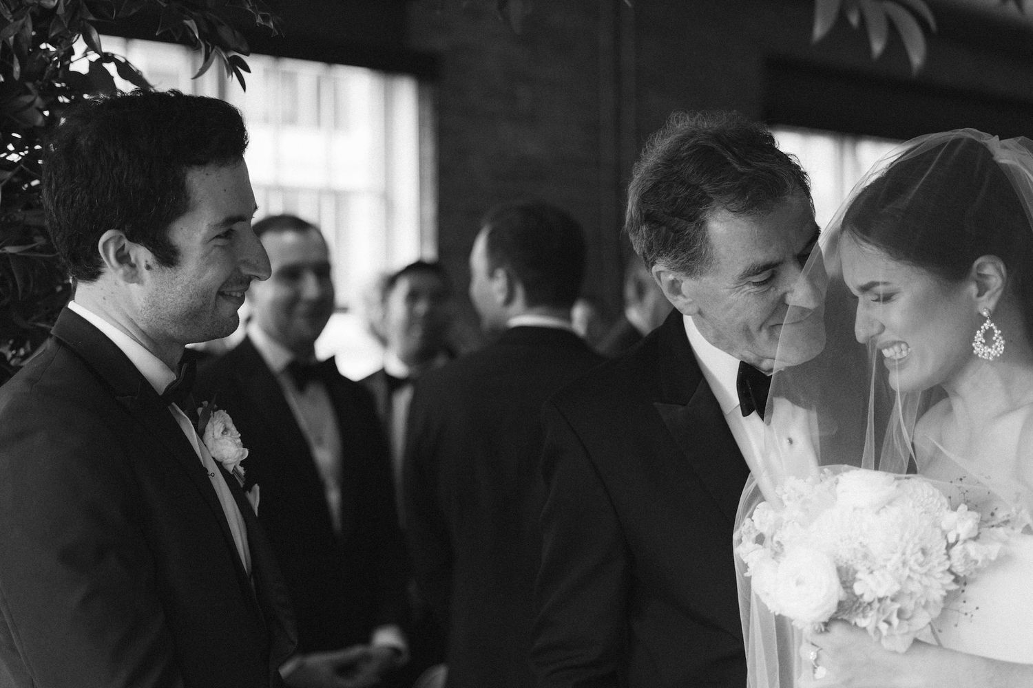 Black and white wedding photo of bride and groom sharing a joyful moment with guests at an elegant indoor ceremony.