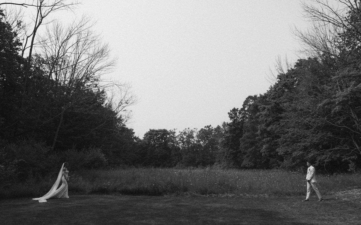 Black and white photo of two people in a open field surrounded by dense trees.