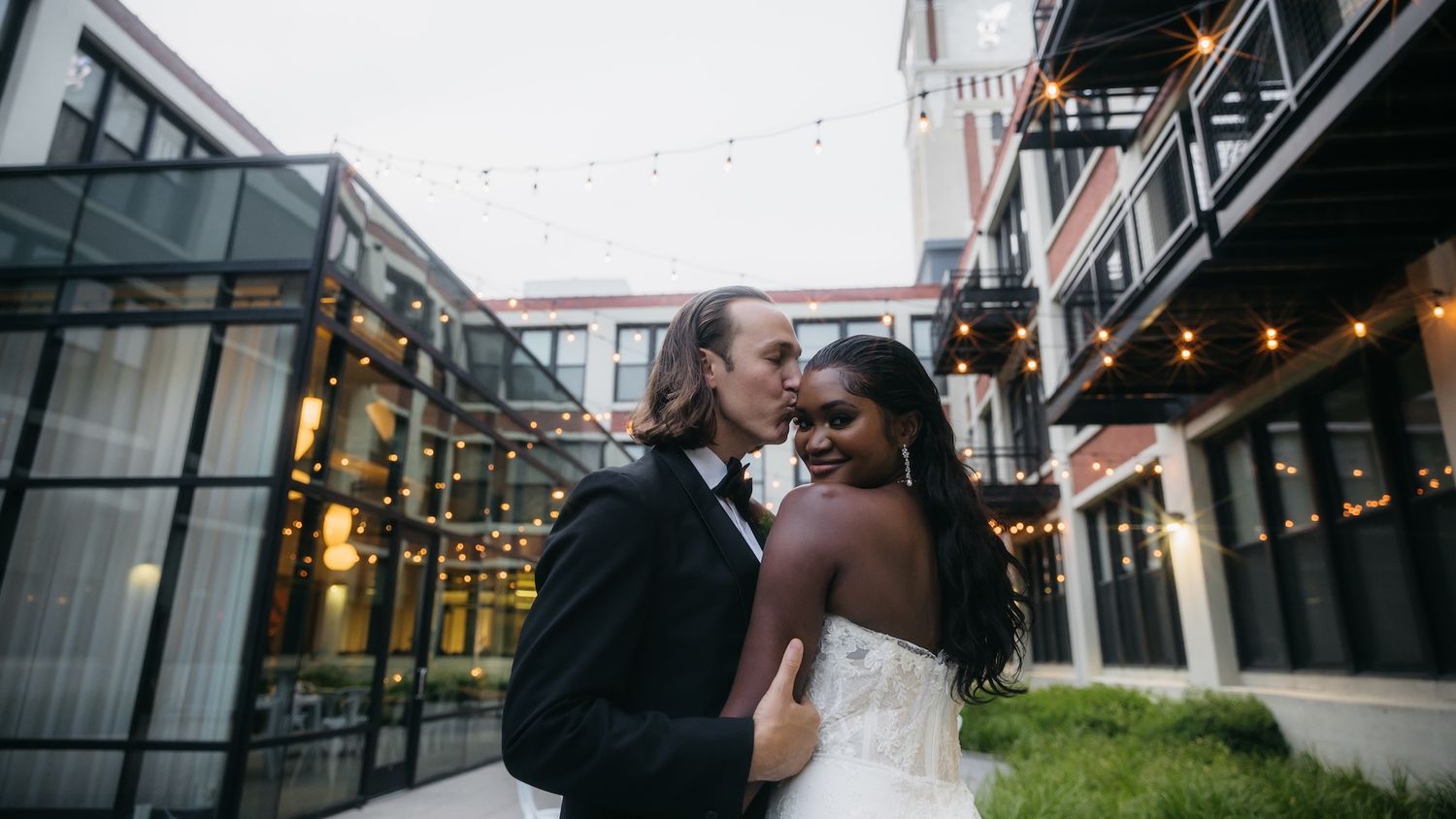 Bride and groom sharing a romantic kiss in an elegant outdoor courtyard with string lights at their wedding.
