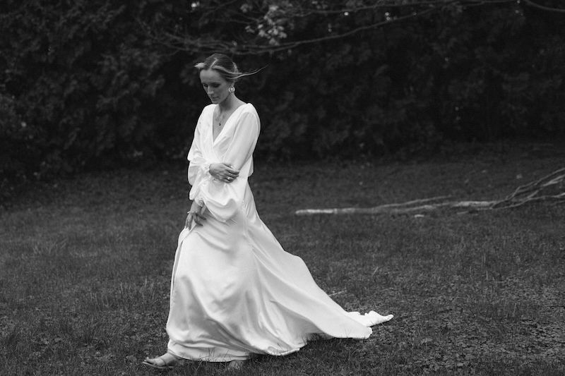 Black and white photo of a bride in a flowing white gown walking gracefully across a lush green lawn.
