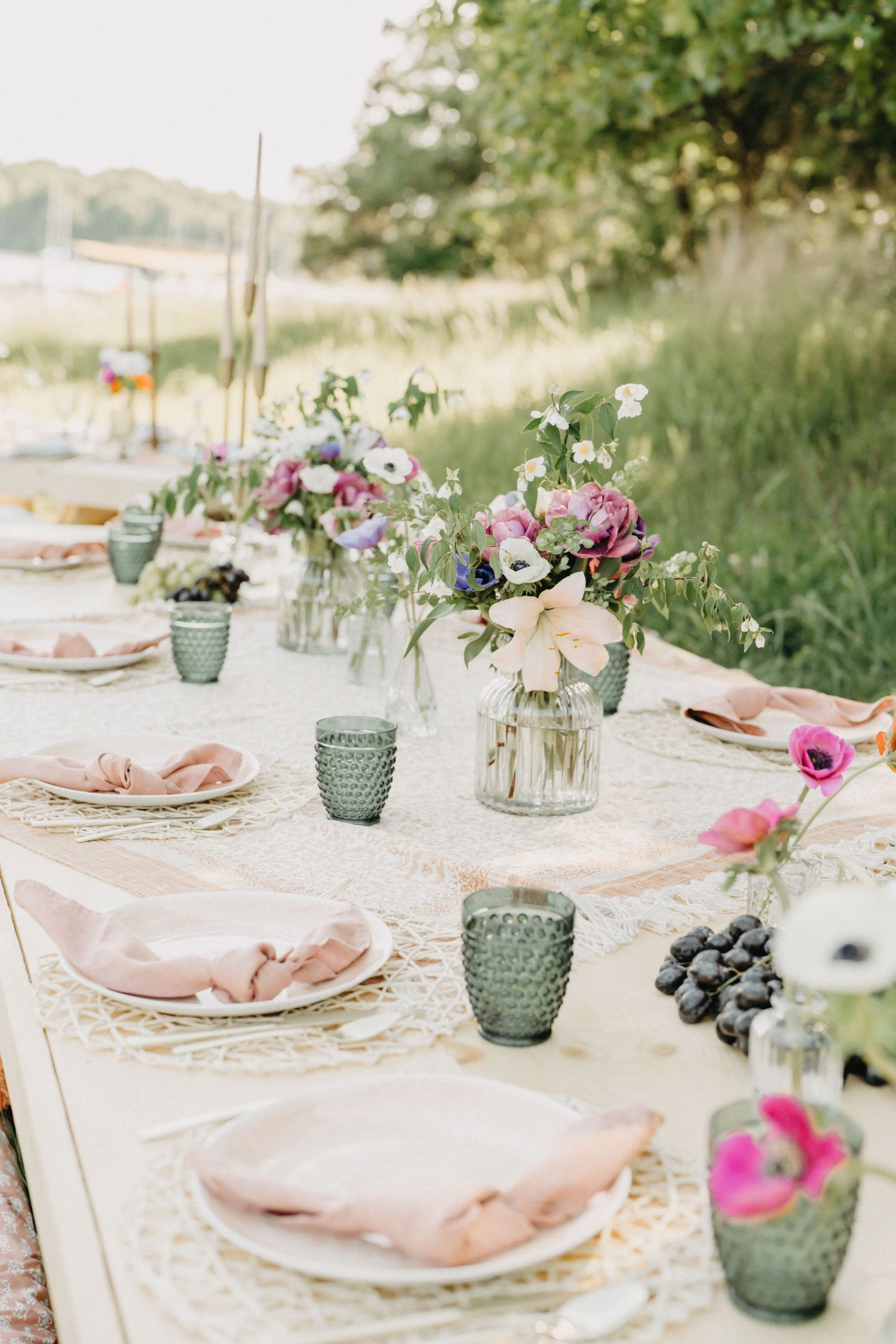 Beautiful outdoor tablescape with pink napkins, green textured glasses, and fresh floral arrangements.