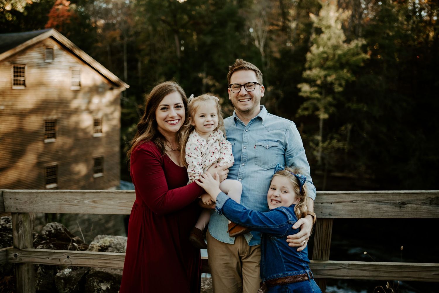 Family wearing coordinated burgundy and blue outfits poses together outdoors during autumn photoshoot.
