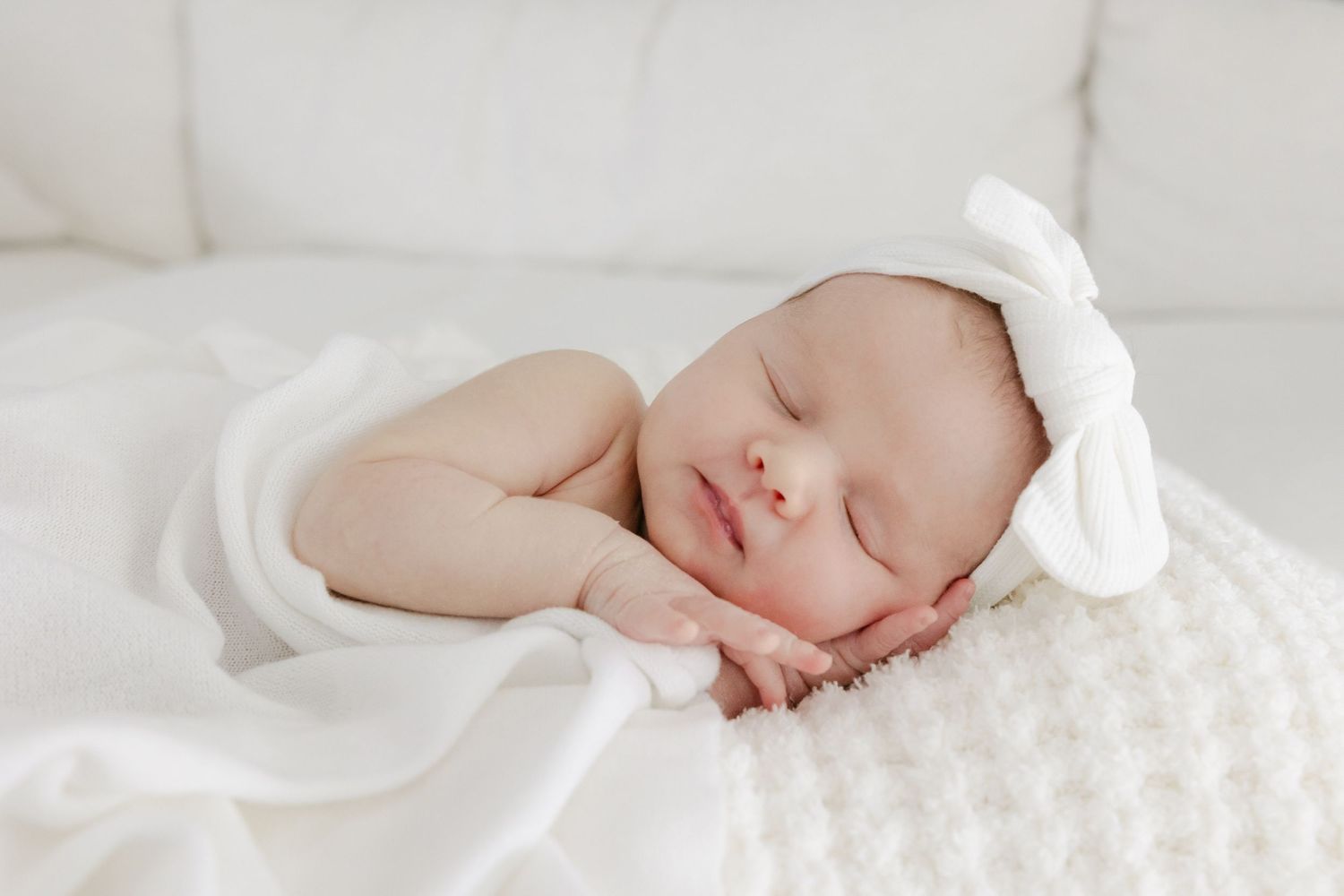 Sleeping newborn baby wrapped in soft white blankets rests peacefully against light backdrop. Connecticut Newborn Photographer.