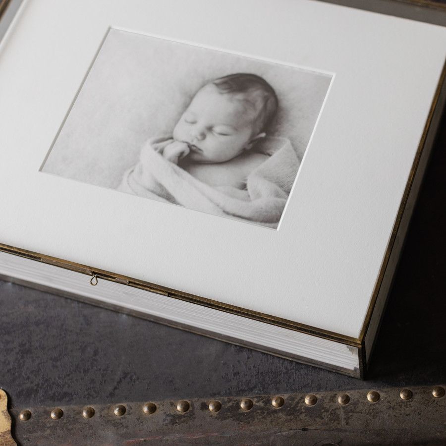 Elegant white photo box with black and white newborn baby portrait, displayed on rustic surface.