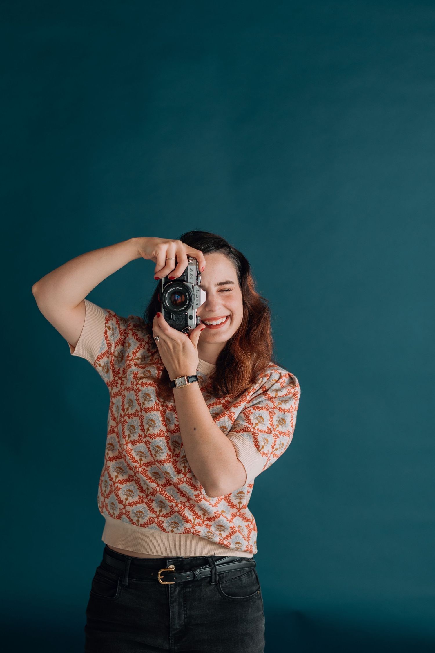 Person holding vintage camera and smiling against teal background.