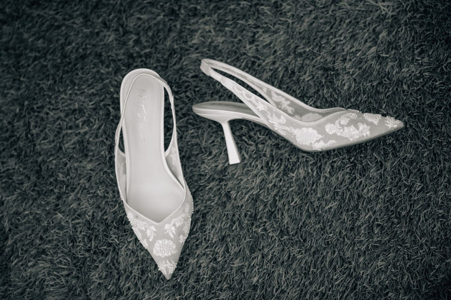 Elegant white lace bridal slingback heels displayed on dark carpet.