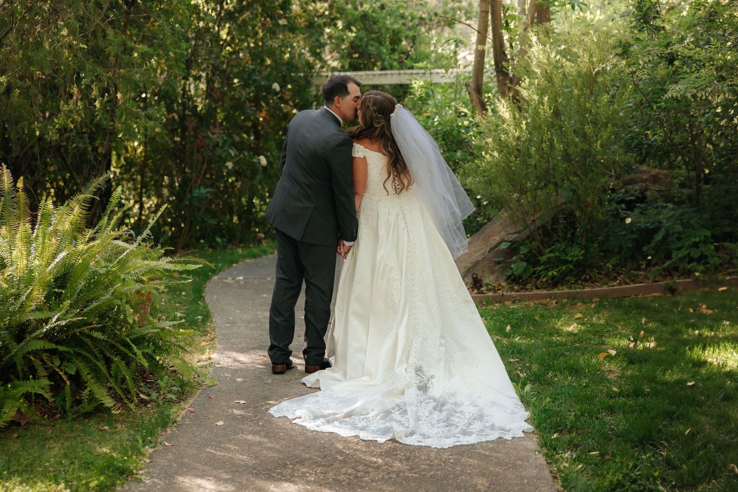 Elegant wedding couple walking through a garden path surrounded by natural greenery.