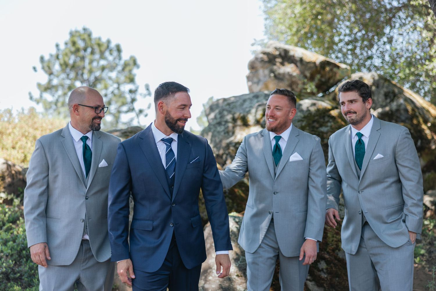 Groomsmen in coordinating gray and navy suits laughing together outdoors.