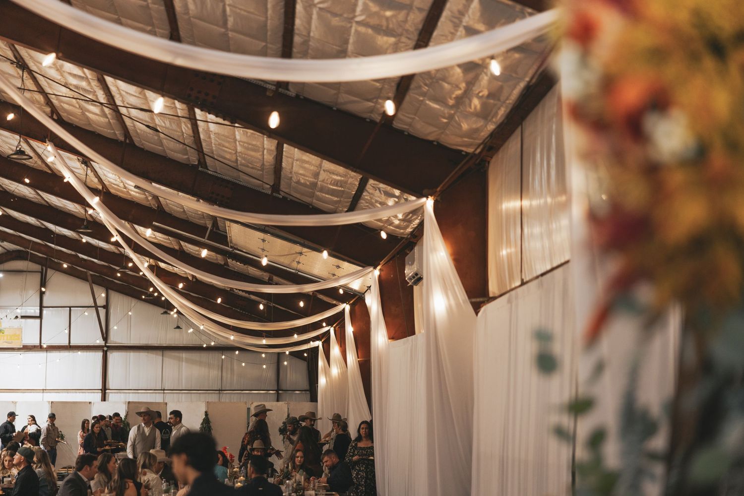 Rustic wedding venue interior decorated with string lights and exposed wooden beams creates a warm ambiance.